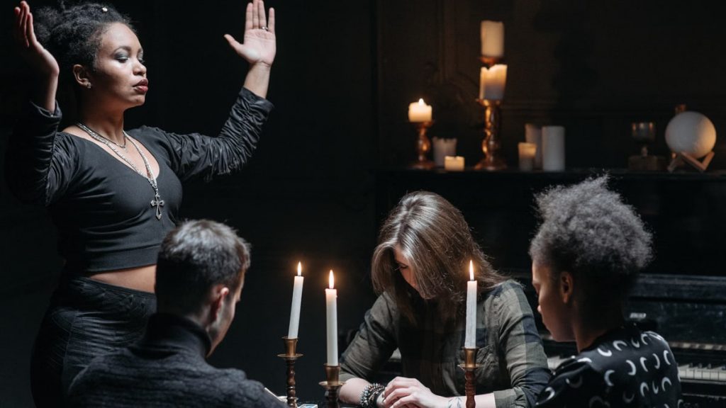 People engaging in a mystical seance with candles and a medium leading the session.